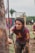 A person is participating in an outdoor obstacle course, grabbing onto a rope with determination. Their clothing is covered in mud, indicating a challenging and intense competition environment. In the background, there are palm trees and obstacle structures, contributing to the rugged and adventurous setting.