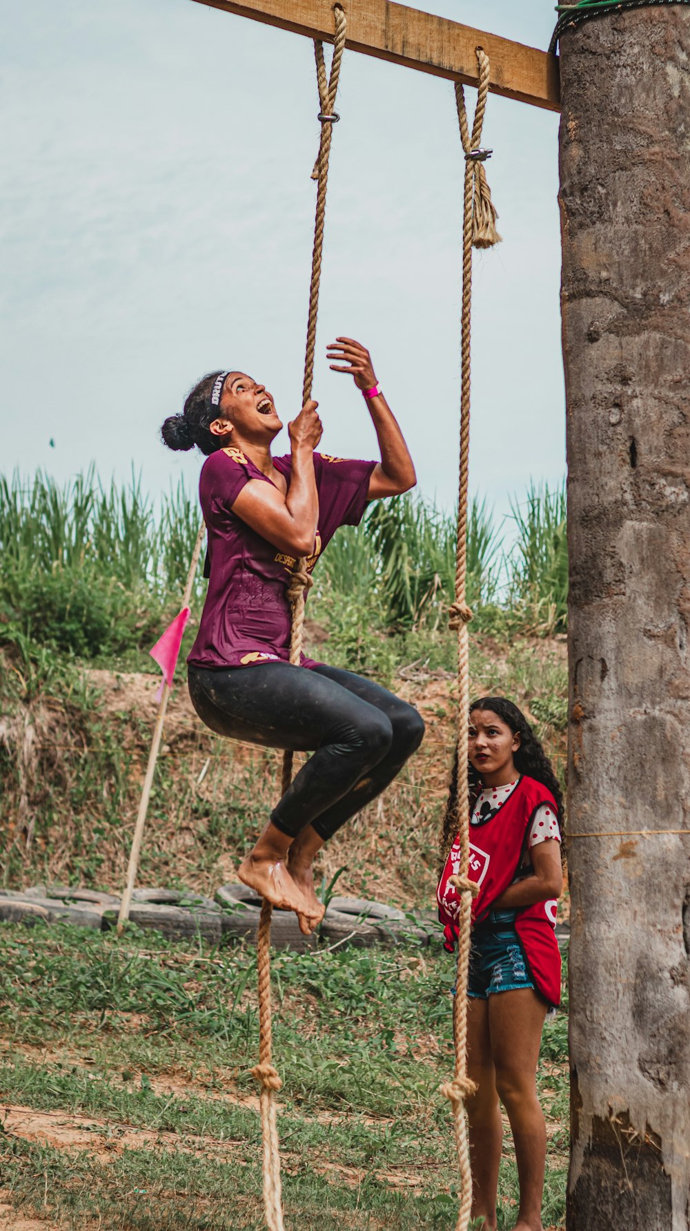 woman in pink tank top and black leggings climbing on brown rope during daytime