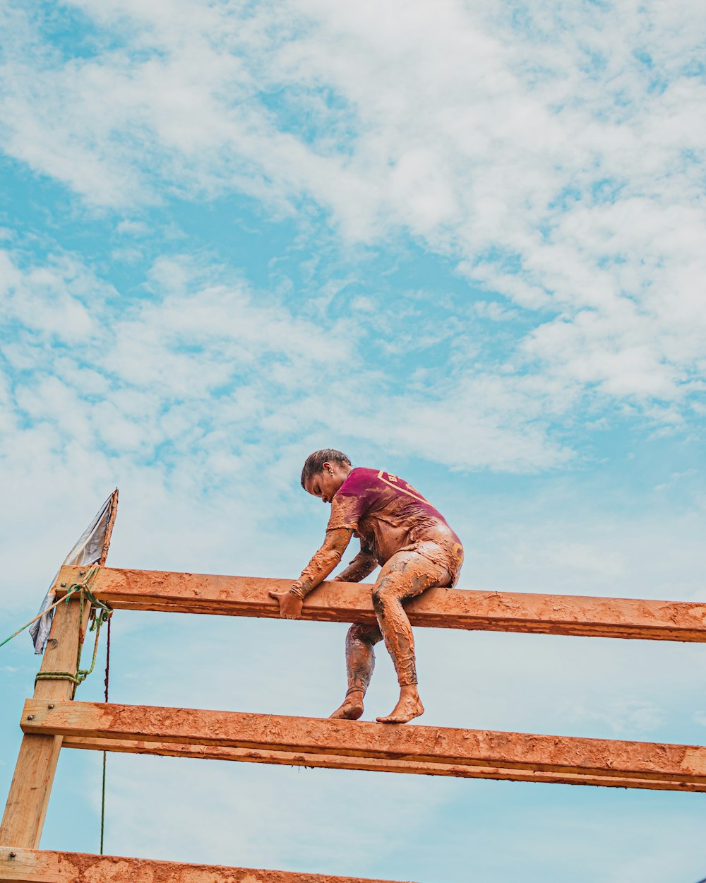 man in red shirt and brown pants jumping on brown wooden fence under blue sky during