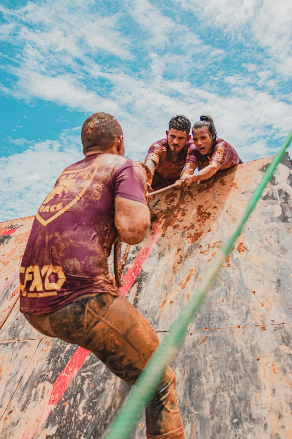 man in black and orange tank top and brown pants climbing on green metal bar during