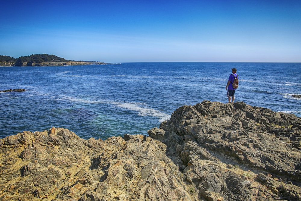 man in black shirt standing on rock formation near sea during daytime