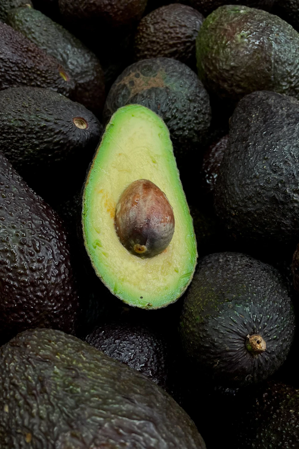 Pile of fresh whole avocados with one halved