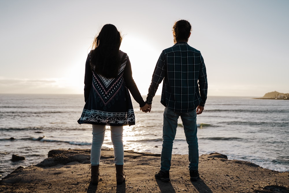 man and woman holding hands while walking on beach during daytime