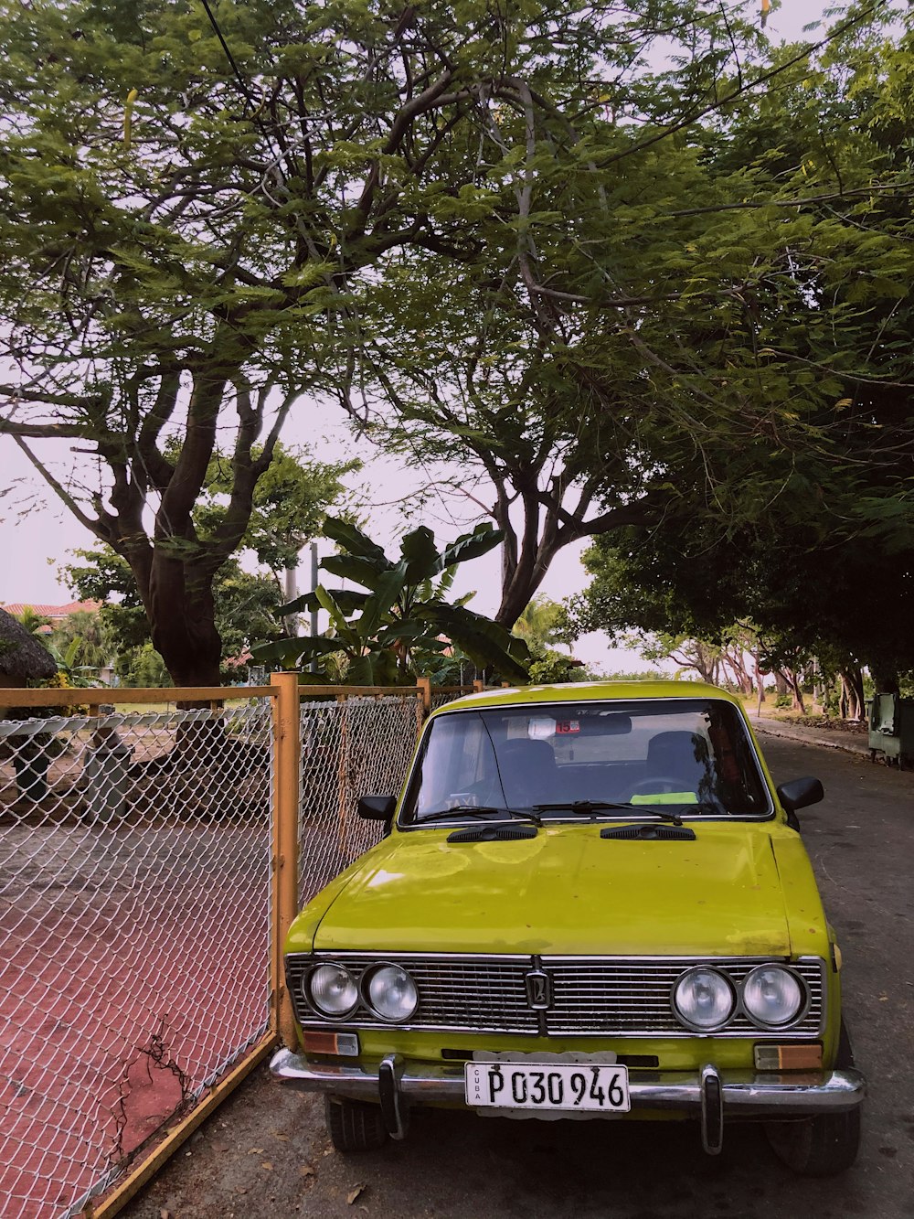 green car parked beside gray metal fence