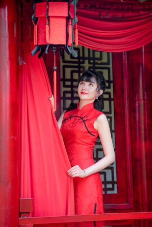 A model wearing a sleek, tailored cheongsam standing by a sunlit window with minimalist decor.