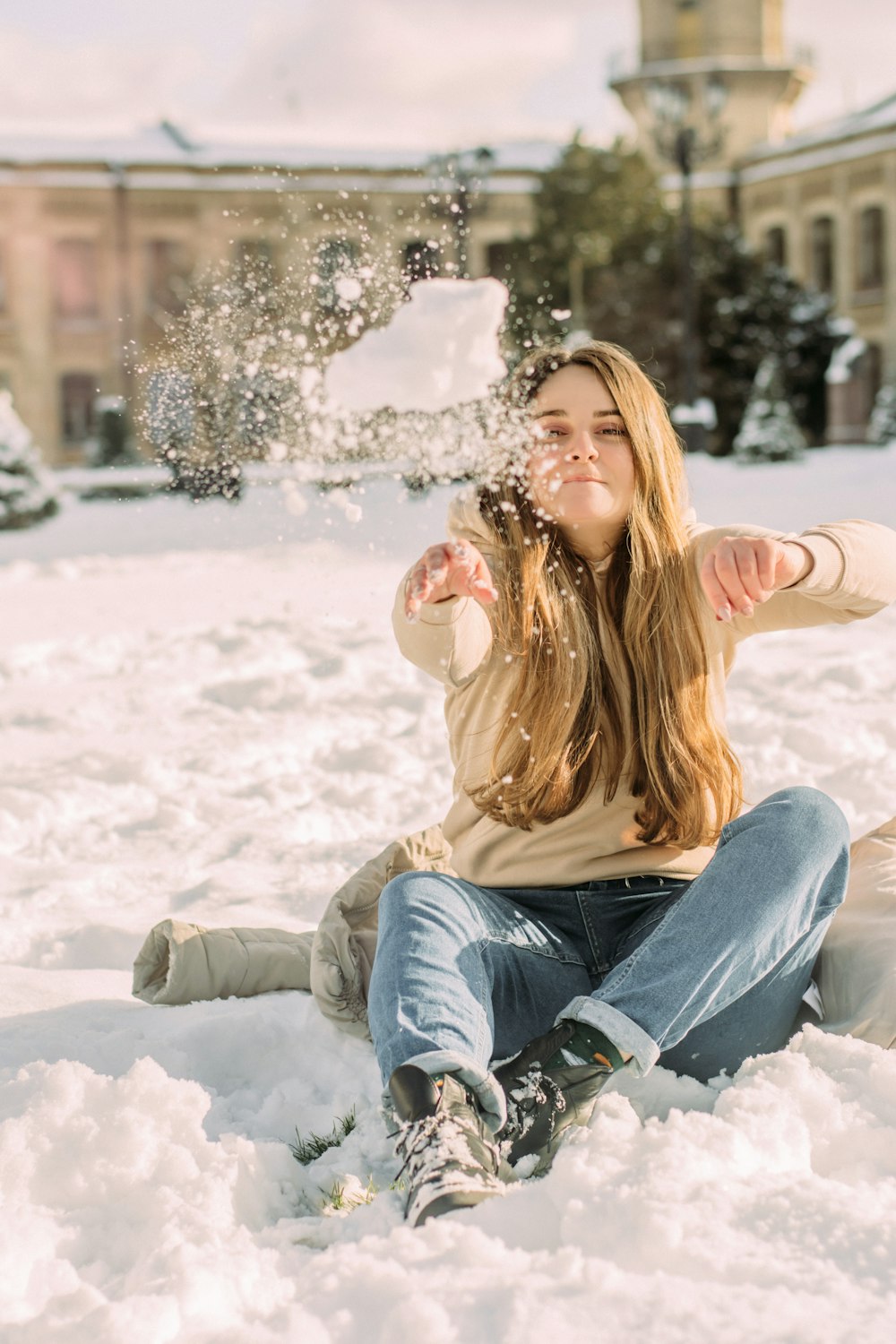 woman in beige long sleeve shirt and blue denim jeans sitting on snow covered ground during