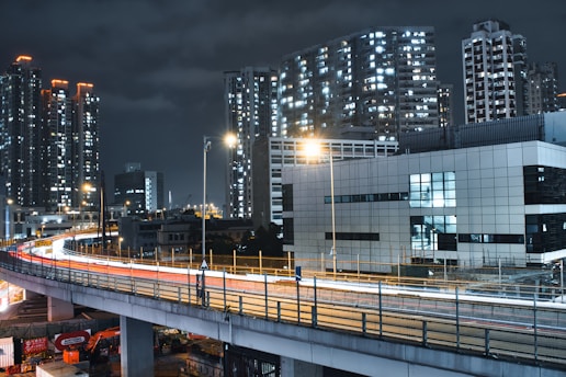 A sleek city skyline at night with glowing light streaks weaving through tall buildings.