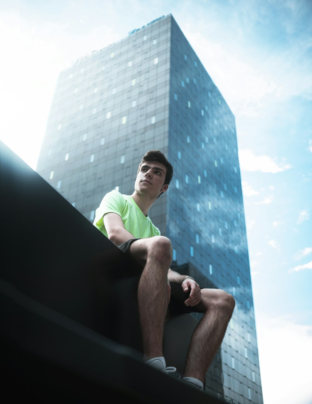man in green t-shirt sitting on black concrete wall