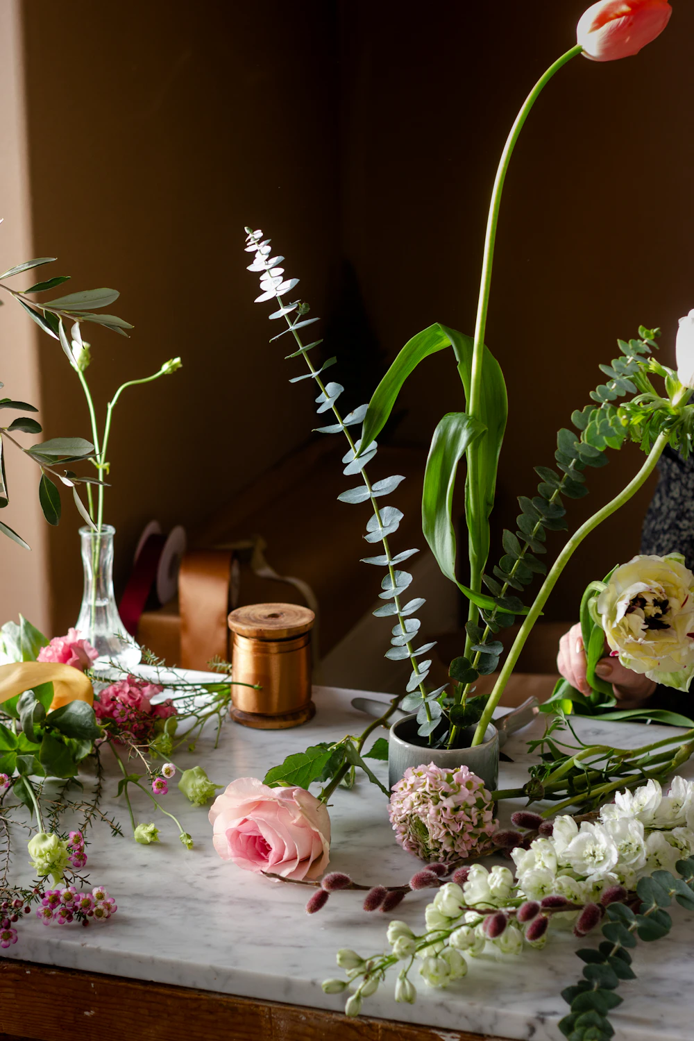 A studio bench with eucalyptus, tools, and a vase of stems