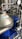 A complex assembly of stainless steel industrial machinery with pipes and valves, featuring a control gauge and warning signs. The machinery components are metallic with blue accents, indicating a possible connection to liquid processing or fluid control.