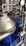 A complex assembly of stainless steel industrial machinery with pipes and valves, featuring a control gauge and warning signs. The machinery components are metallic with blue accents, indicating a possible connection to liquid processing or fluid control.