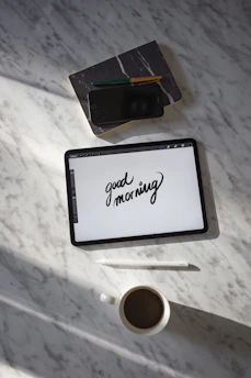 black tablet computer beside white ceramic mug on white table