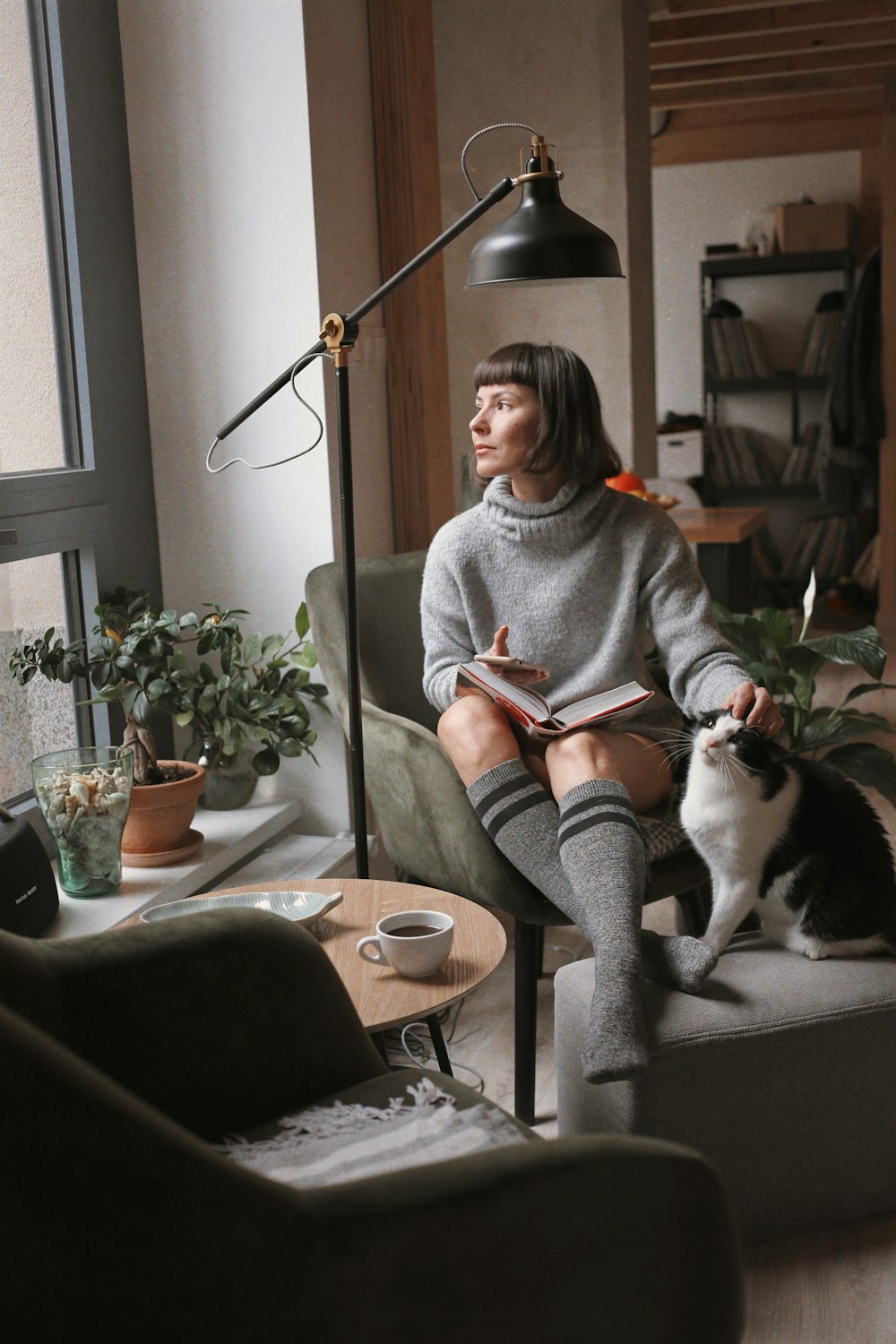 Mujer en suéter gris sentada en la silla al lado del gato blanco y negro