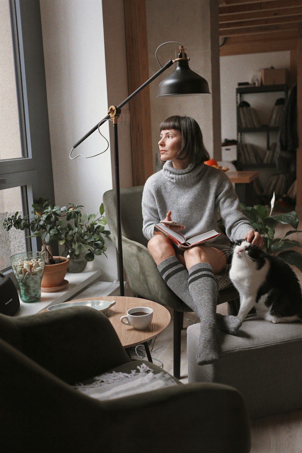woman in gray sweater sitting on chair beside black and white cat