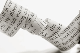 A close-up of a strip of paper that appears to be curled or twisted, featuring black printed text on a white background. The focus is on the text, showing various printed words.