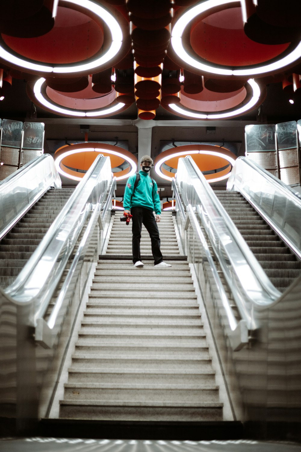 woman in red jacket and blue denim jeans walking on escalator