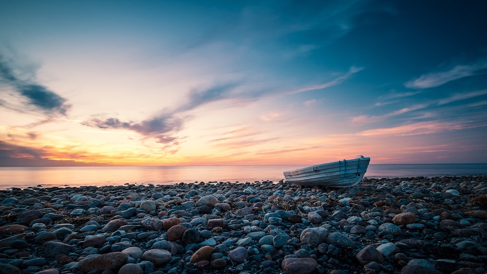 white boat on sea shore during sunset