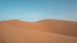 Wide shot of a small group navigating winding tracks through vast Sahara dunes.