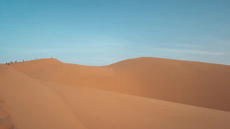 A small group trekking through vast desert dunes under a deep red sky.