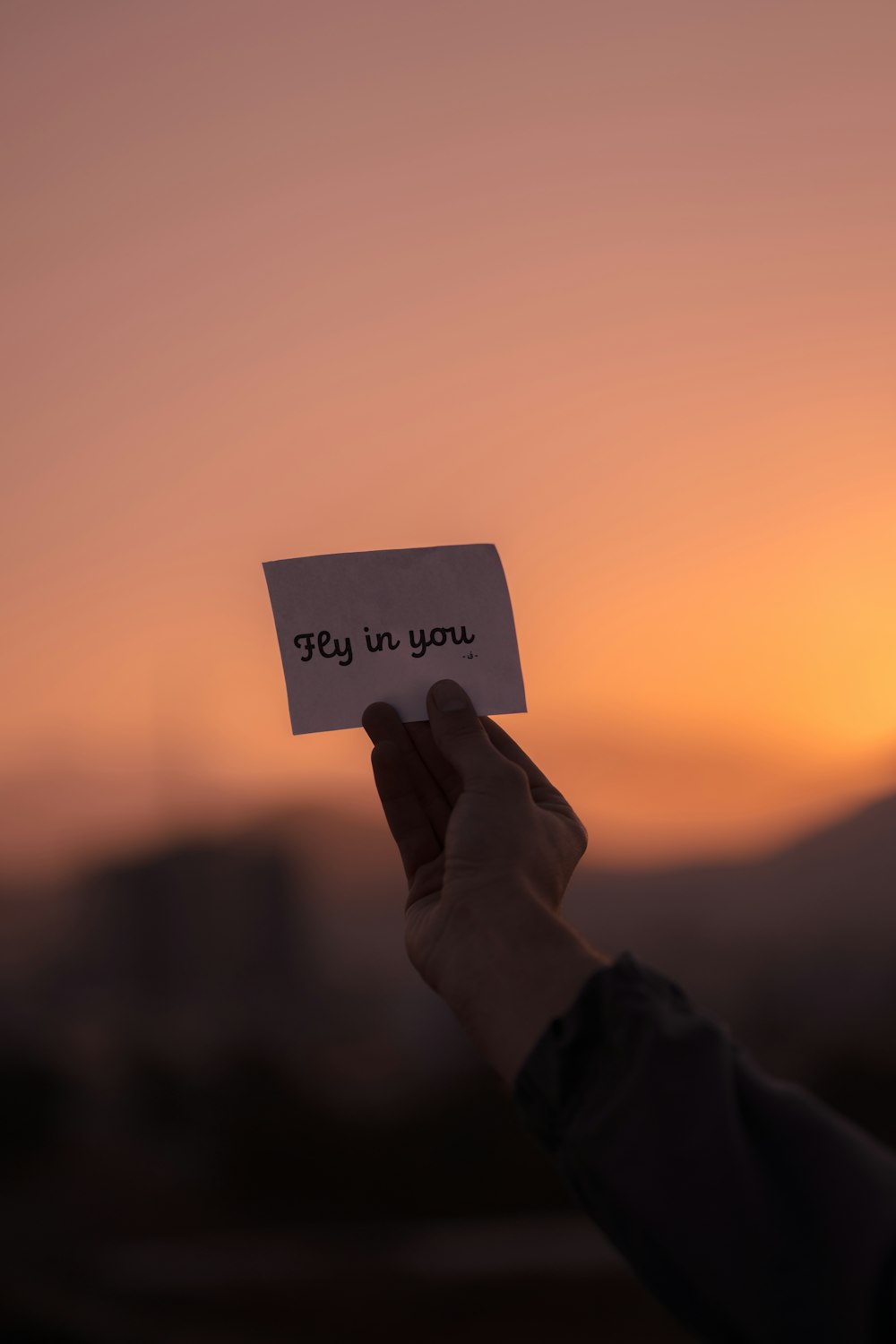 a person holding a piece of paper with the words fly in you written on it