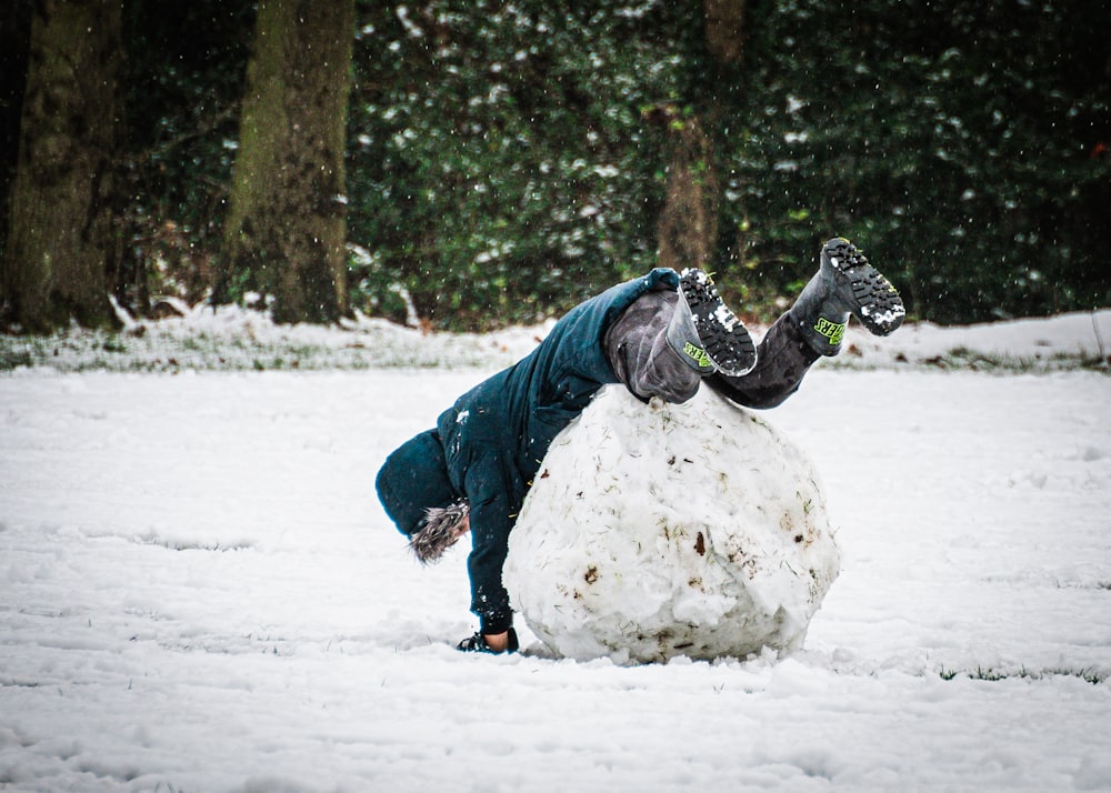 昼間、雪に覆われた地面で遊ぶ青いジャケットと灰色のズボンを着た人