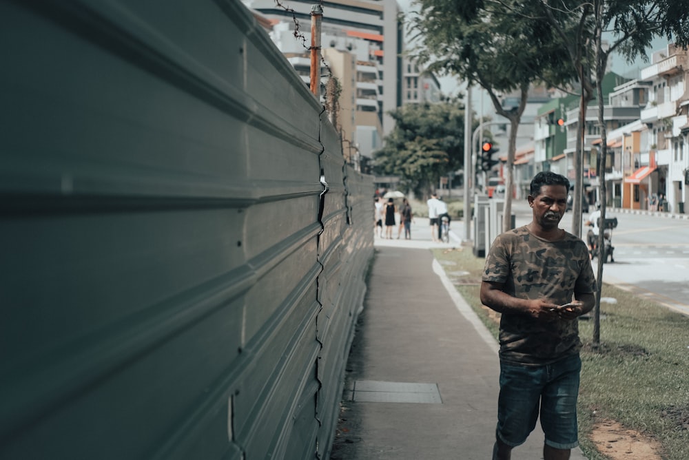 man in brown and black camouflage shirt and blue denim jeans standing on sidewalk during daytime