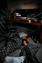 A cozy streamer setup featuring vintage computer gear surrounded by plush pillows and indie game posters.