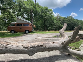 A cozy camper van parked in a lush green forest clearing under a bright blue sky.
