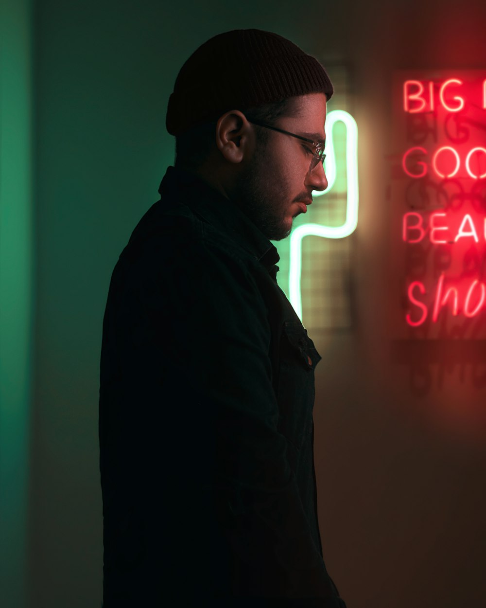 man in black jacket standing near neon sign
