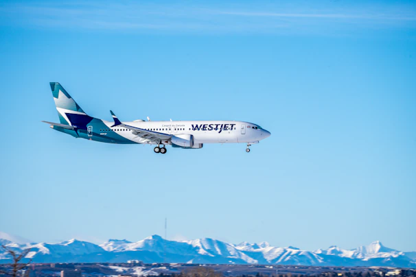 A sleek airplane taking off against a clear blue sky over mountains.
