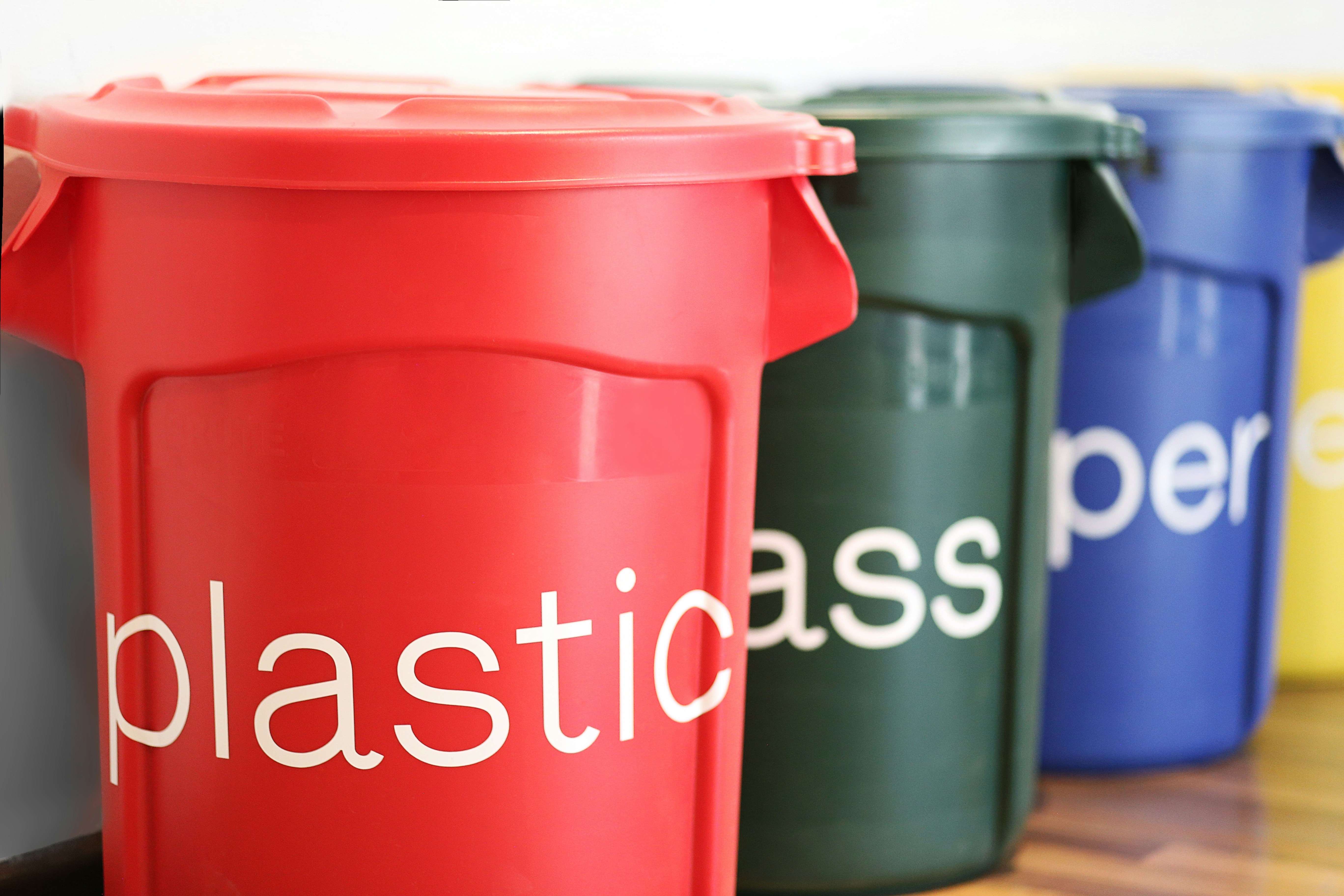 Colourful recycling bins in a row with sorted materials — green for glass, blue for paper, yellow for plastic — in a bright clean facility