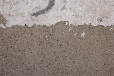 A textured wall with a rough, concrete surface on the lower half and a worn, white plaster section above. A faint, dark curved line runs across the upper portion, suggesting possible graffiti or a mark.