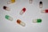 Several capsules are arranged on a white surface. These capsules come in various colors including red, green, yellow, and orange. Each capsule has a happy face drawn on it, giving them a friendly and playful appearance.