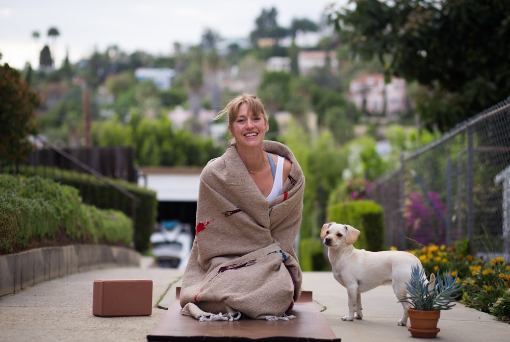 woman in brown robe sitting beside white short coated dog during daytime