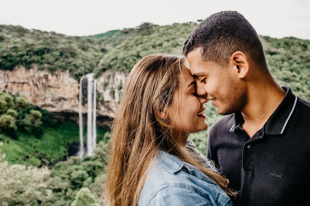 man and woman kissing near green trees during daytime