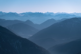 Layers of misty mountains recede into the distance, creating a breathtaking depth of field. The scene is tranquil, with gentle blue hues dominating the landscape.