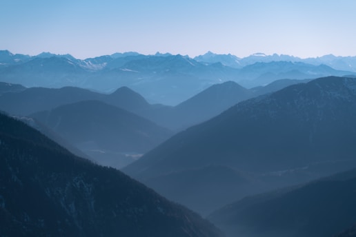 Layers of misty mountains recede into the distance, creating a breathtaking depth of field. The scene is tranquil, with gentle blue hues dominating the landscape.