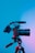 A professional camera mounted on a tripod against a gradient blue and pink background, with lighting creating a dramatic effect on the equipment.