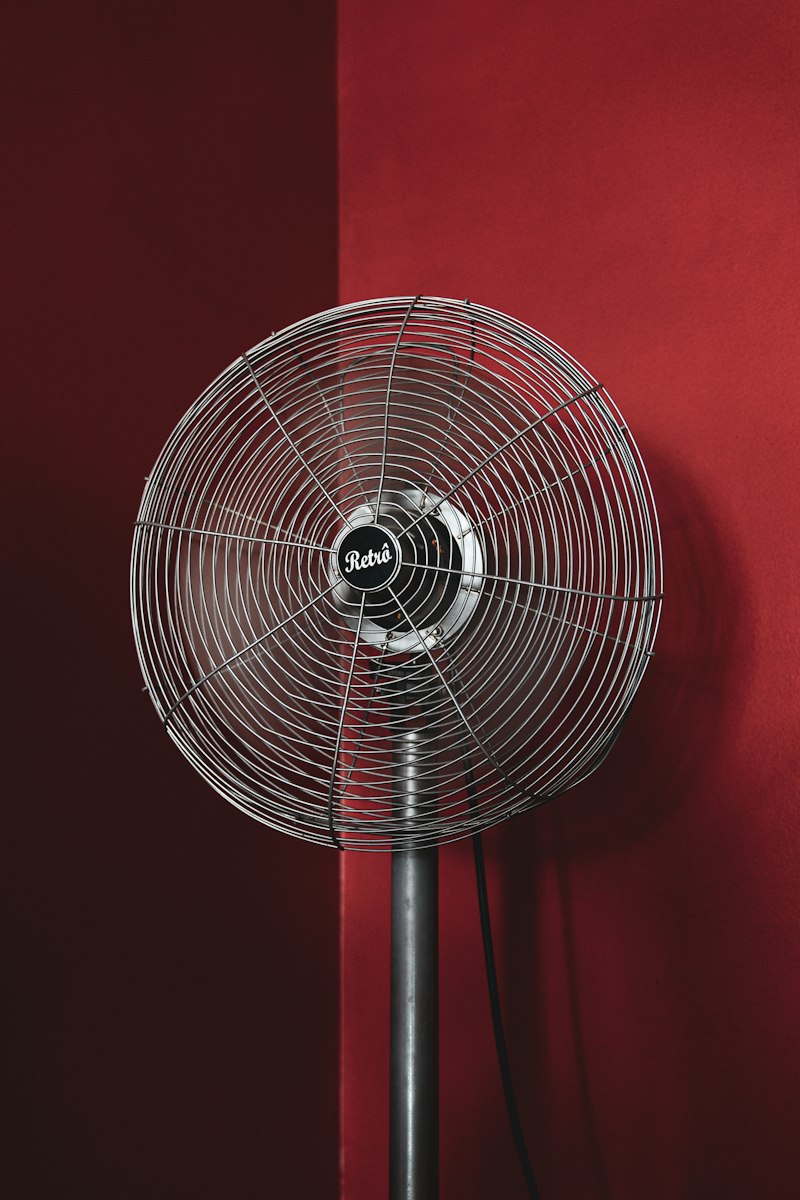 Ventilador de pie metálico encendido frente a una pared roja