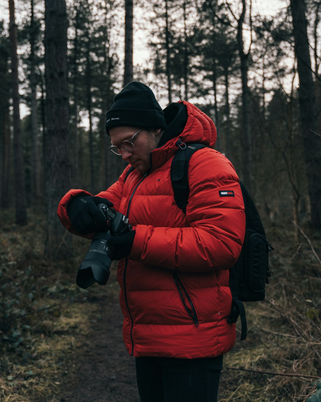 man in red jacket and black knit cap standing in forest during daytime