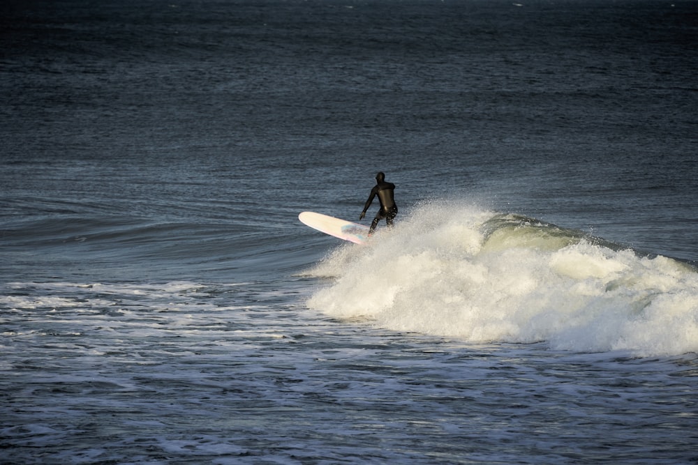 man in black wet suit riding white surfboard on sea waves during daytime