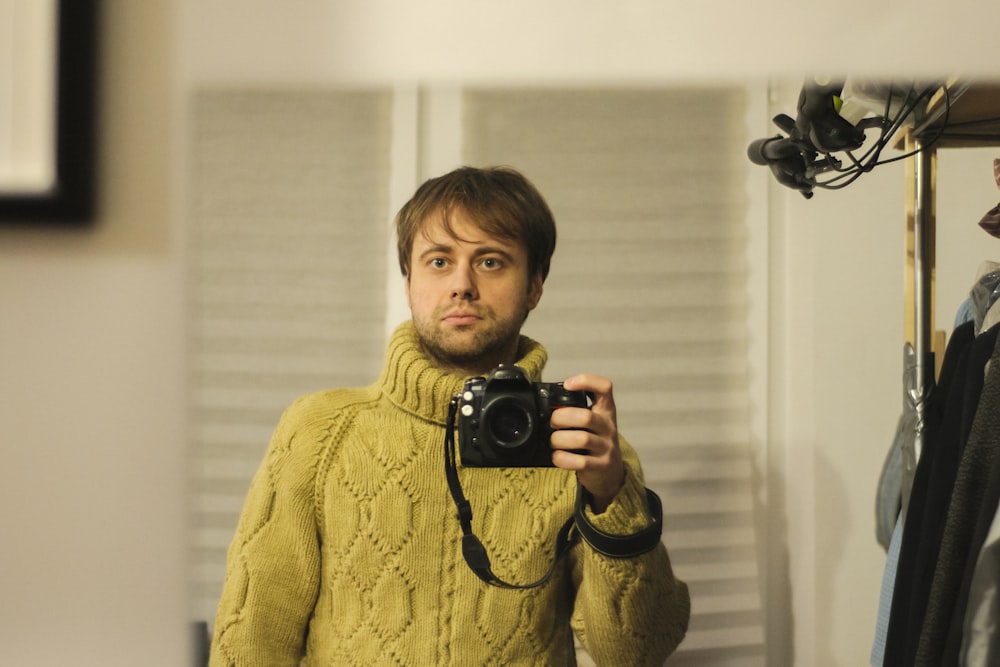 boy in yellow sweater holding black camera