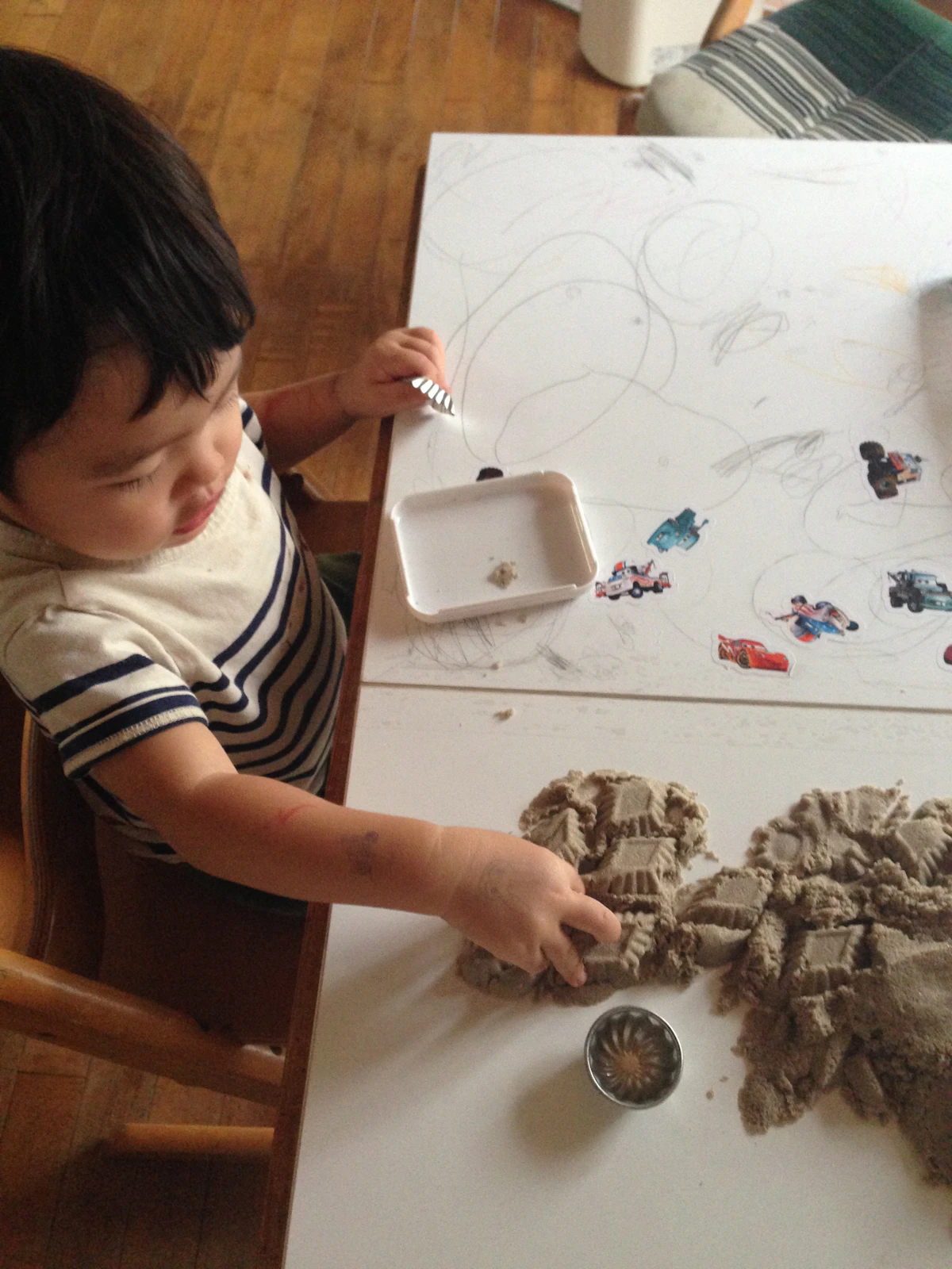 Toddler standing at a low table scooping and pouring into a sensory bin