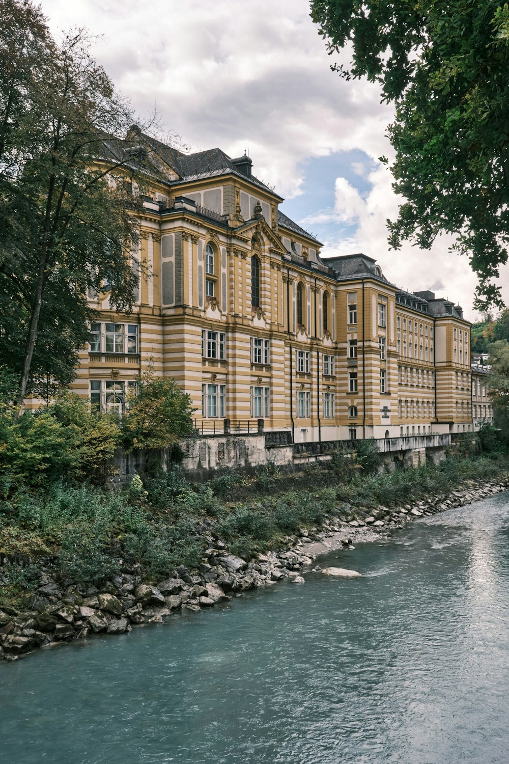 Braunes Betongebäude in Flussnähe unter weißen Wolken und blauem Himmel tagsüber