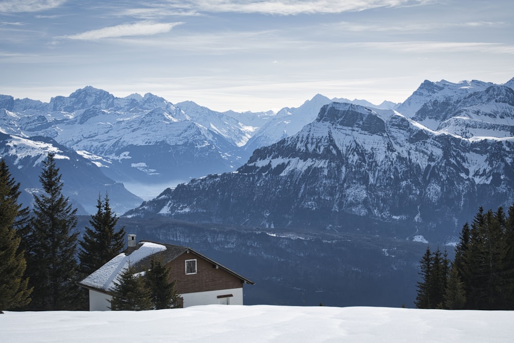 brown wooden house on snow covered ground near snow covered mountain during daytime