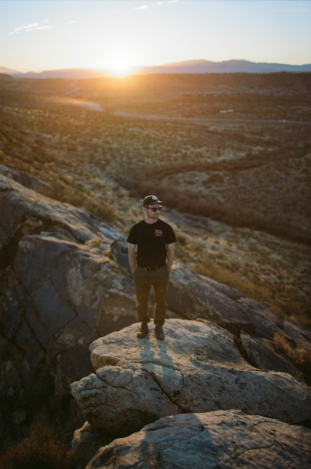 man in black t-shirt standing on rock formation during sunset