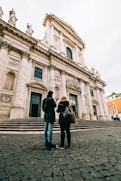 man and woman standing in front of white concrete building during daytime