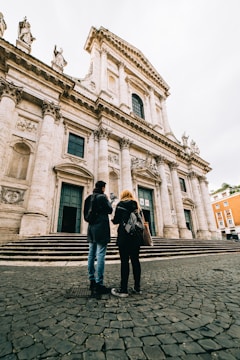man and woman standing in front of white concrete building during daytime