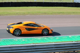 A bright orange sports car speeding on a racetrack under clear skies.