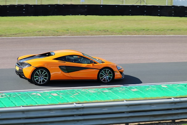 A bright orange sports car speeding on a racetrack under clear skies.